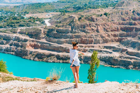 A slender girl in a white shirt walks alone be the sandy career. Against the background of mountains and a blue azure lake. Georgia summertimeの写真素材