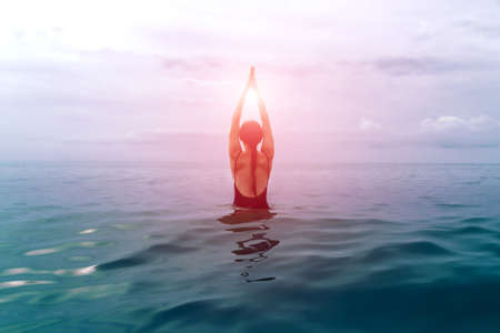 A girl in a black swimsuit practices yoga in the sea. namasteの写真素材