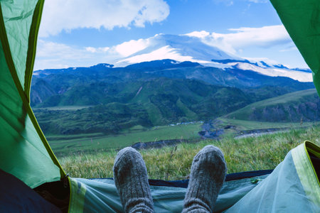 Legs in knitted gray woolen socks. Morning view from the tent on the Caucasus mountains to Elbrus....
