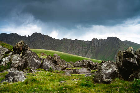 Stones on a green meadow against the backdrop of the Caucasus Mountains. Cloudy weather. Beautiful landscapeの写真素材