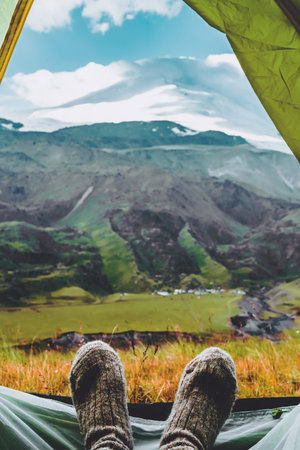 Legs in knitted gray woolen socks. Morning view from the tent on the Caucasus mountains to Elbrus. Travel lifestyle. Beautiful landscape Vertical photoの写真素材