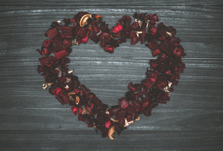 Background with gray wooden planks, leaves and red dry flowers forming a heartの写真素材