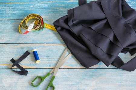 Tools for sewing: the fabric, scissors, pins, tape measure on blue wooden background top view, flat...