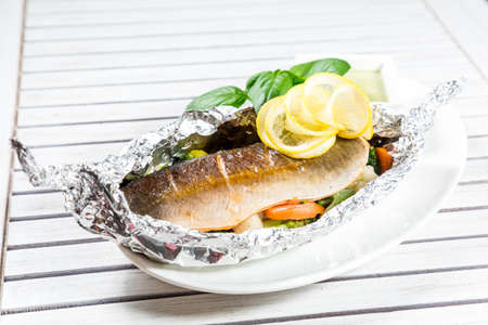 Tasty baked fish with grilled vegetables on  plate on wooden table close-upの写真素材