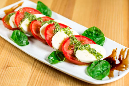Caprese salad with mozzarella, tomato, basil and balsamic vinegar arranged on white plateの写真素材