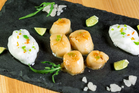 Studio close up of seared scallops, garnished with greens and sauceの写真素材