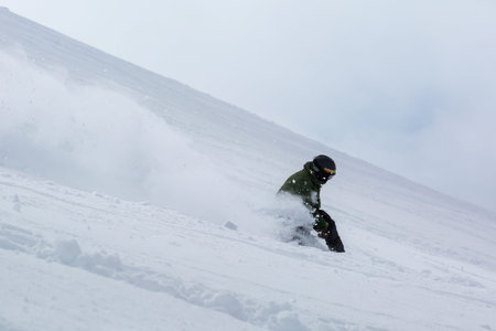 Male snowboarder snowboarding on fresh snow on ski slope on Sunny winter day in the ski resort in...