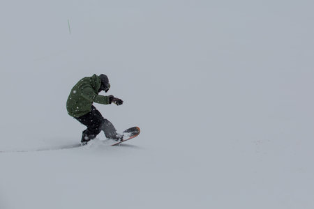 Male snowboarder snowboarding on fresh snow on ski slope on Sunny winter day in the ski resort in Georgiaの写真素材