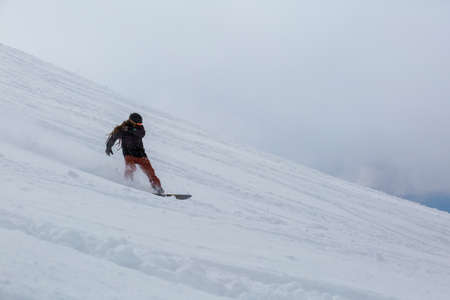 Male snowboarder snowboarding on fresh snow on ski slope on Sunny winter day in the ski resort in Georgiaの写真素材