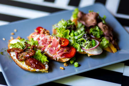 three sandwiches with bacon and fresh vegetables on vintage  blue plate. Close-up.の写真素材