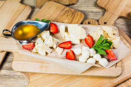Delicious Cheese heaven. Cheese Mix, gouda cheese, cheese parmesan, feta cheese and strawberries with sauce on a wooden boardの写真素材