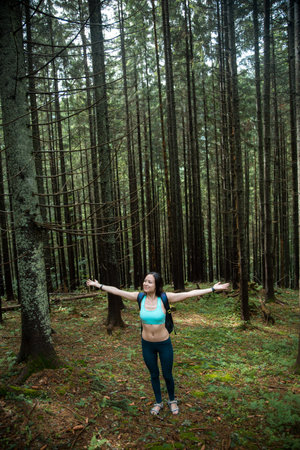 Young beautiful girl tourist with a Hiking backpack and a sports figure walking in the woods