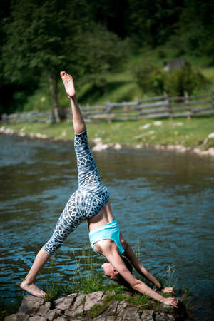 Young beautiful girl with nice body stands on the head during yoga on the shore of a mountain river.の写真素材