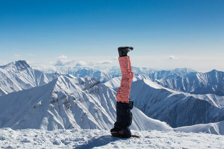 Girl in warm clothing standing on his head on the white snow in the mountains