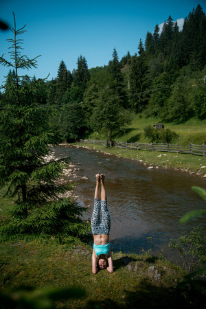 Young beautiful girl with nice body stands on the head during yoga on the shore of a mountain river.