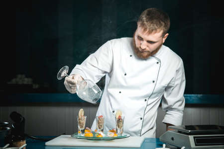 Cheerful bearded chef cook cooking while cooking meals in the kitchenの写真素材