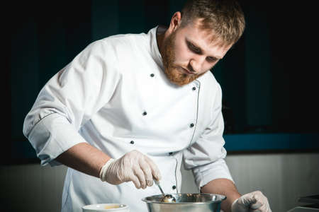 Cheerful bearded chef cook cooking while cooking meals in the kitchenの写真素材