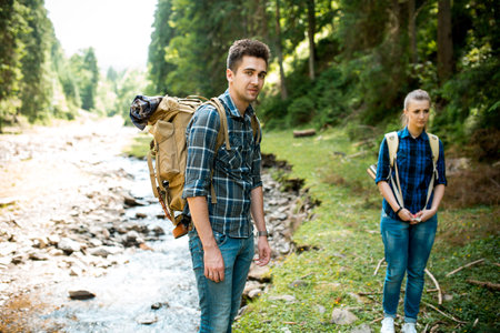 Man and woman tourists walking hand in hand through the woods in the mountains by the river