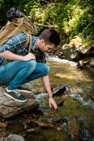 beautiful young guy tourist on the shore of a mountain riverの写真素材