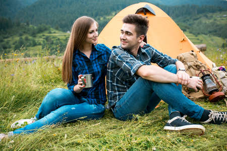 A couple of tourists in time of the hike, sit outside the tent, mountain scenery. The guy hugs the girl. The concept of love and recreationの写真素材