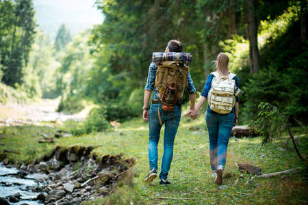 Man and woman tourists walking hand in hand through the woods in the mountains by the riverの写真素材