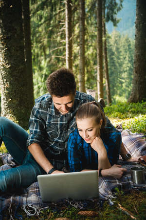 A guy and a girl tourists rest in the forest and looking in laptopの写真素材