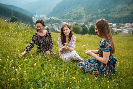 Girls girlfriends in dresses sitting on the grass outdoors in a beautiful mountain meadowの写真素材