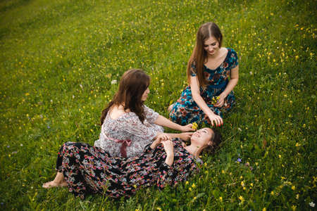 Girls girlfriends in dresses sitting on the grass outdoors in a beautiful mountain meadowの写真素材
