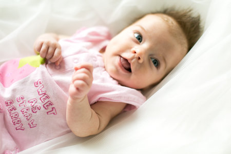 Funny and cute smiling baby looking at camera. An adorable laughing newborn girl close up.