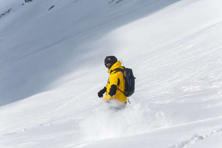 Male snowboarder snowboarding on fresh snow on ski slope on Sunny winter day in the ski resort in Georgiaの写真素材