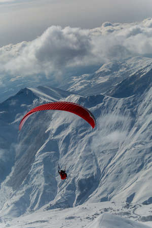 Parachute sky-diver flying in clouds above mountains with fresh snow on Sunny winter day in the ski resort. Travel adventure concept. space for textの写真素材