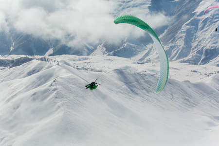 Parachute sky-diver flying in clouds above mountains with fresh snow on Sunny winter day in the ski resort. Travel adventure concept. space for textの写真素材