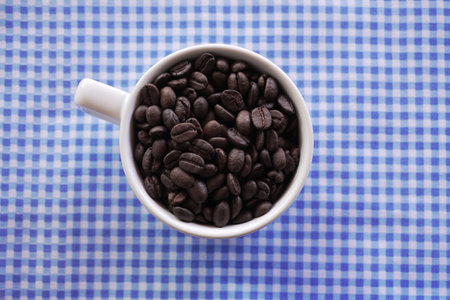 Flat lay of coffee beans in white ceramic cup on tableclothの写真素材