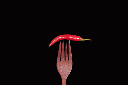 Red hot chili pepper on a wooden fork, isolated on black backgroundの写真素材