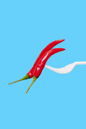 Red hot chili peppers on a fork on a blue background. Minimal food concept.の写真素材