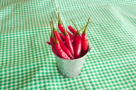 Red hot chili peppers in a small bucket on a green tableclothの写真素材