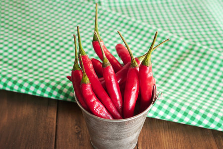 Red hot chili peppers in a bucket on a green tablecloth.の写真素材