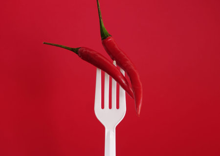 Red hot chili peppers on a white plastic fork against a red background