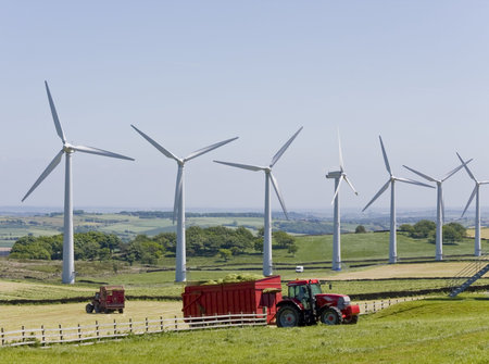 Windmills in windfarm with tractors working in foreground