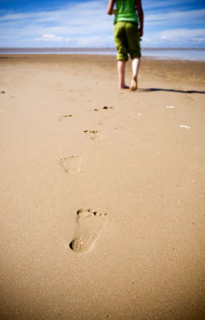 Young girl walking on the beach leaving footprints in the sandの写真素材