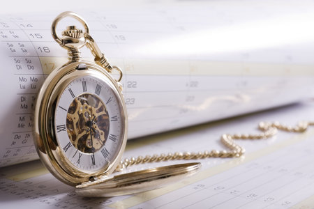 Business scheduling concept - high key shot of gold pocket watch on calendar with copy spaceの写真素材