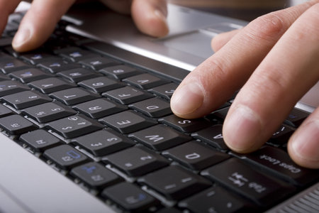 Close up of mans hands typing on a laptop keyboard