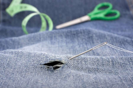 Needle and thread to repair a ripped pair of denim jeansの写真素材
