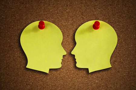 Head shape paper note reminder with thumb tack pin on cork board concept for face off, health care, dementia, memory, discussion and business meetingの写真素材