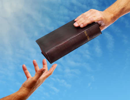 Passing over the bible hand giving a bible to another reaching outの写真素材