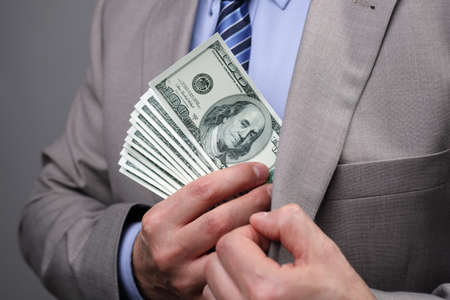 Man putting money in suit jacket pocket concept for corruption, bribing, paying or business wealthの写真素材
