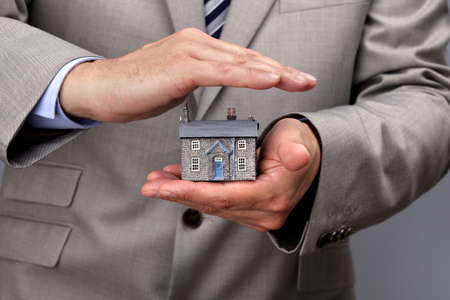 Businessman protecting a model house, real estate or insurance conceptの写真素材