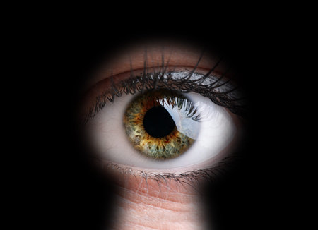 Womans eye peeking through a keyhole concept for curiosity, stalker, surveillance and security