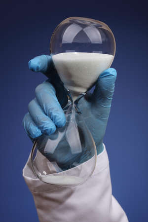 Doctor or surgeon holding an hourglass concept for long delays for medical procedure and hospital waiting listの写真素材