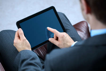 Businessman with finger touching screen of a digital tablet whilst sitting on a sofaの写真素材